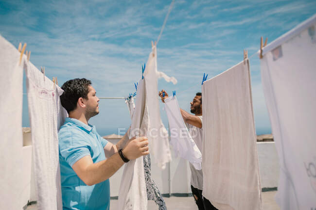 Vielrassige Männer hängen Kleider bei hellem Tag auf — Stockfoto