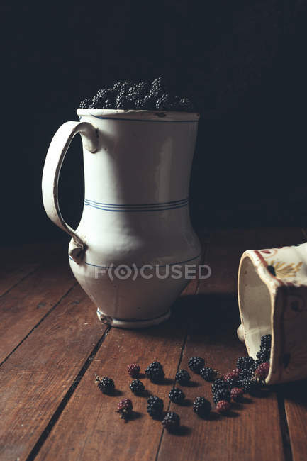 Moras sabrosas y apetitosas maduras en mesa de madera y en decantadores blancos en sombra - foto de stock