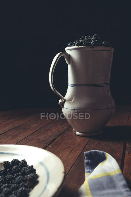 Vintage jag with ripe blackberries and plate on wooden table — Stock Photo