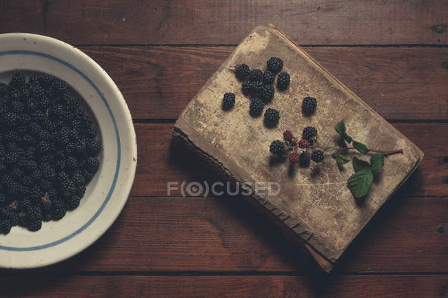 Ripe blackberries in bowl and vintage book on wooden table — Stock Photo