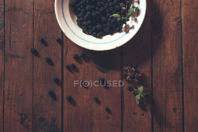 Ripe blackberries garnished by leaves in bowl — Stock Photo