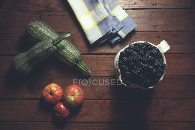 Спелые ежевики украшены овощами в миске на деревянном фоне — стоковое фото