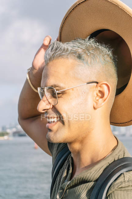 Vue latérale de Jeune homme avec des lunettes levant son chapeau — Photo de stock