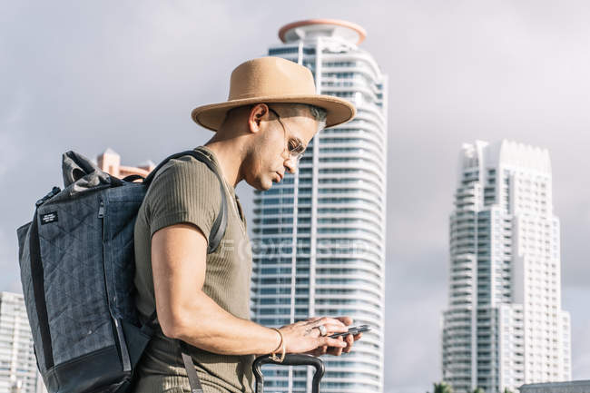 Человек в шляпе и рюкзаке ищет направление по телефону — стоковое фото