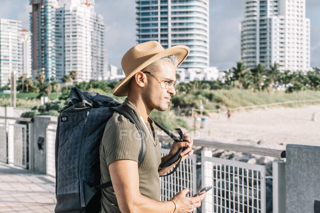 Профіль молодого чоловіка з рюкзаком, що тримає смартфон — стокове фото