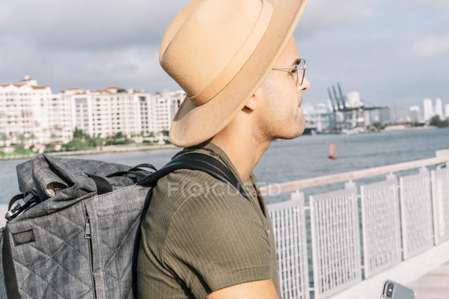 Vista lateral del hombre con buen sombrero y gafas mirando hacia delante portando mochila. - foto de stock