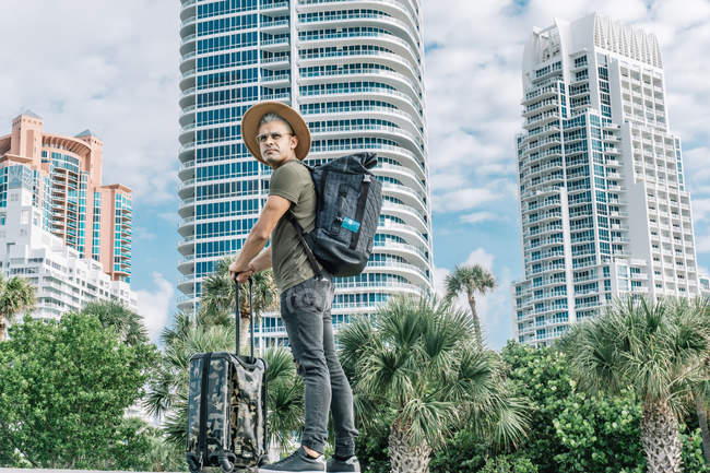 Мандрівник з капелюхом, що носить рюкзак і валізу, шукає напрямки, щоб залишитися в місті — стокове фото