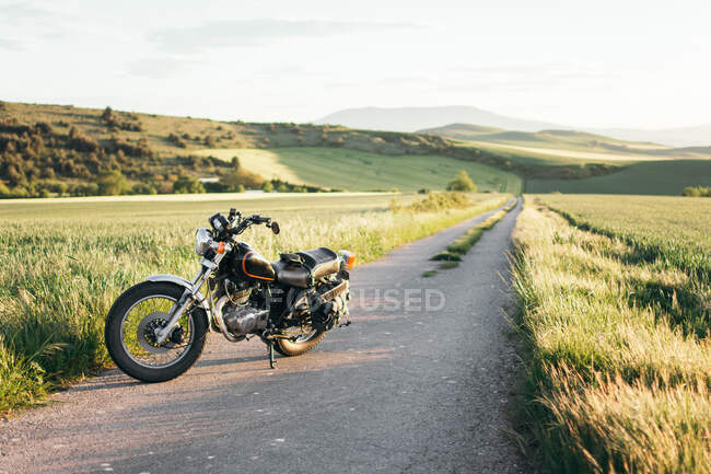 Современный мотоцикл припаркован на асфальтовой дороге возле травянистого поля в солнечный день в спокойной природе — стоковое фото