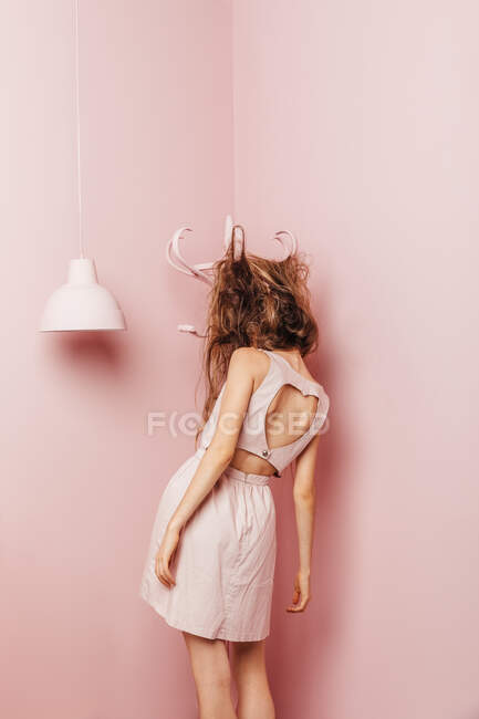Konzeptueller Blick von hinten auf ein Teenager-Mädchen mit wirren Haaren auf rosa Hintergrund — Stockfoto