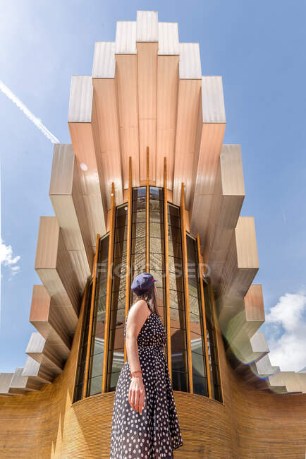 Desde abajo curioso turista de pie y disfrutando de la vista de edificio creativo de forma geométrica compleja con rectángulos - foto de stock
