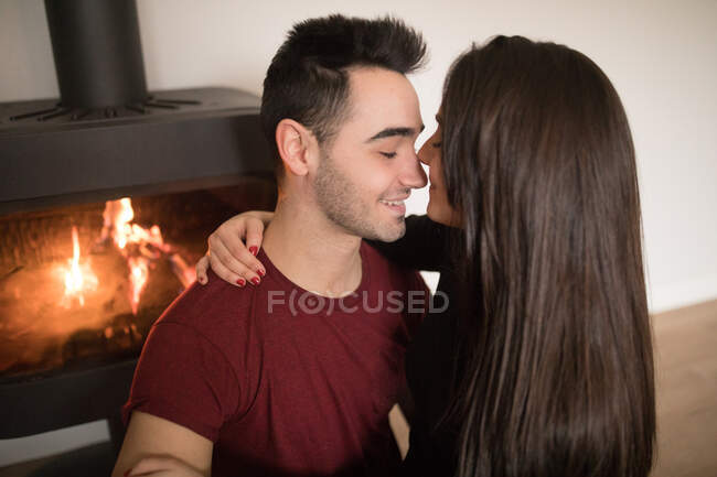 Happy couple in casual clothes embracing each other near fireplace at home — Stock Photo