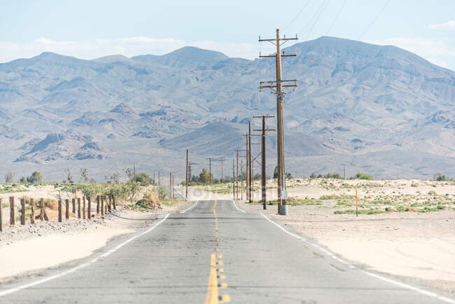 Autopista rural en campo polvoriento con línea eléctrica y cordillera remota en Estados Unidos - foto de stock