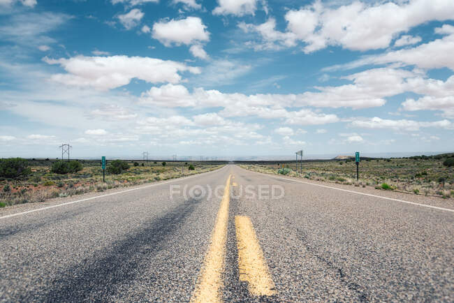 Autopista rural en campo polvoriento con línea eléctrica y cordillera remota en Route 66, USA - foto de stock