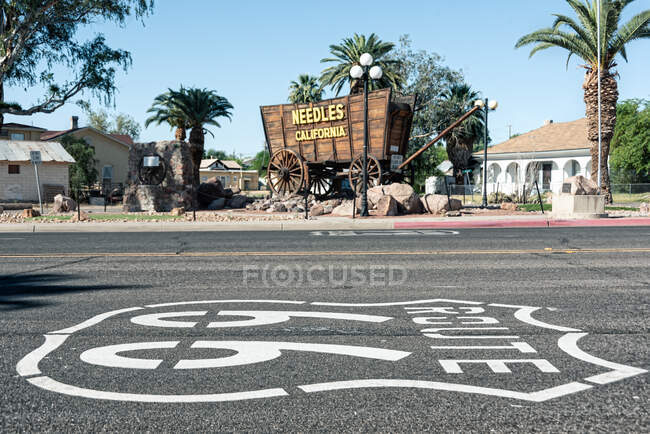 Asphalt road with painted sign and palm trees by cottages on sunny day in Needles, California, USA — Stock Photo