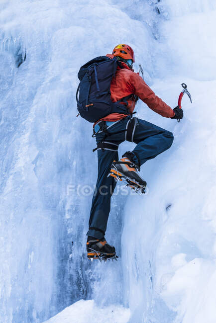 Back view of person in warm clothes with backpack using tools to climb frozen mountain glacier — Stock Photo