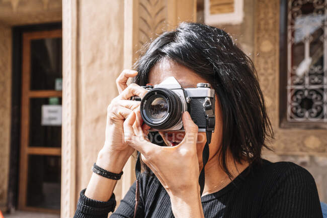 Positive Frau im lässigen Outfit mit Kamera-Einstelloptiken für Fotoshootings, während sie vor dem Café steht — Stockfoto