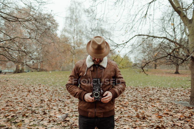 Homem adulto com câmera de foto retro em pé em folhas secas no pacífico parque de outono no outono — Fotografia de Stock