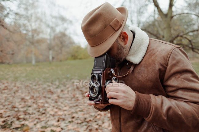 Осінній вигляд дорослого чоловіка з ретро фотокамерою стоїть на сухих листках. — стокове фото
