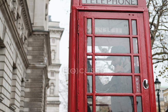 From below traditional red telephone booth located against autumn trees and old buildings on street of London — Stock Photo
