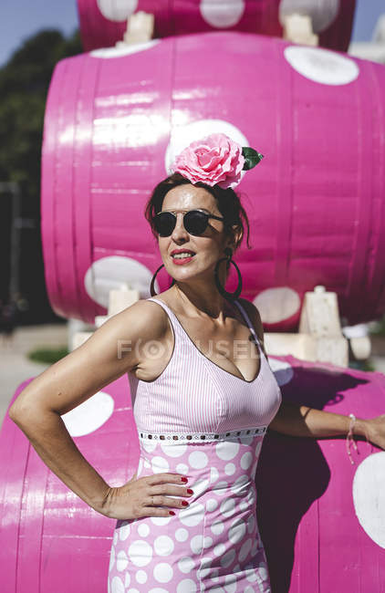 Vue latérale de excentrique curieuse femme en costume rose coloré debout près de beau baril rose vif le jour ensoleillé — Photo de stock