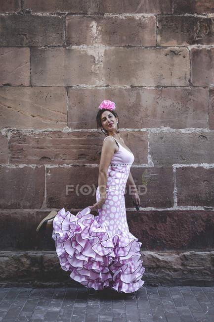У сонячний день дивись на ексцентричну веселу жінку в рожевому вбранні, усміхаючись і танцюючи під цегляною стіною. — стокове фото