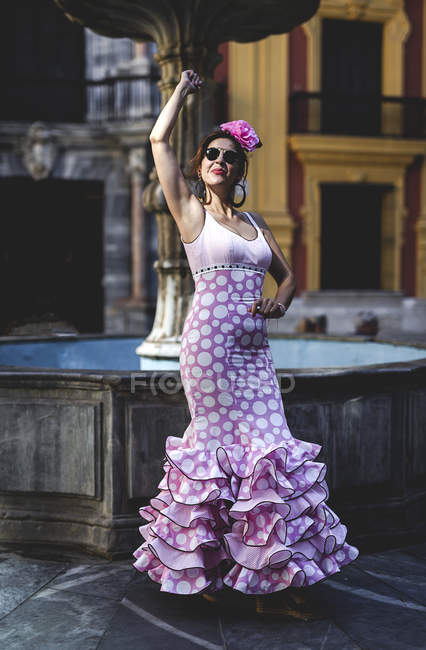Femme excentrique ravie en costume rose coloré souriant et dansant par fontaine le jour ensoleillé — Photo de stock