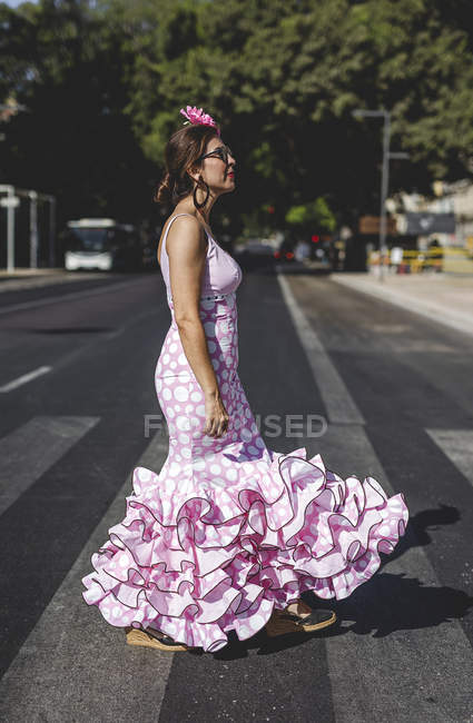 Vista laterale di donna felice eccentrica in costume rosa colorato sorridente e passeggiando lungo il passaggio pedonale nella giornata di sole — Foto stock