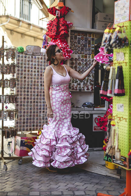 Curiosa donna felice in costume rosa colorato sorridente e controllo merci a bancarella souvenir ispanico nella giornata di sole — Foto stock