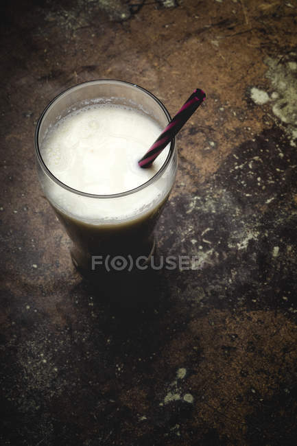 Высокий стакан белого молока с яркой полосатой соломой на столе на черном фоне — стоковое фото