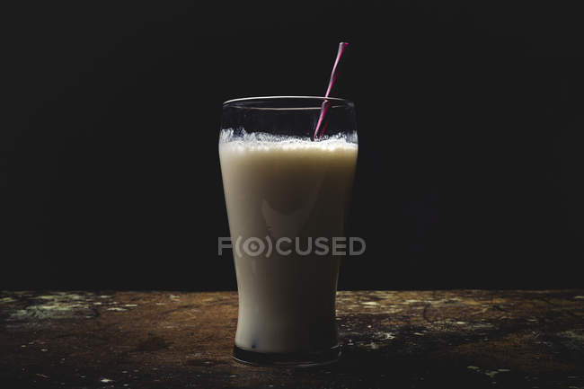 Bicchiere alto di latte bianco con paglia a righe brillanti sul tavolo su sfondo nero — Foto stock