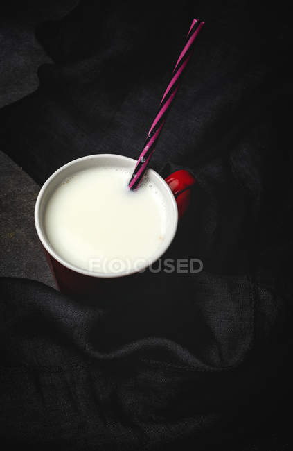 Copo de leite branco com palha listrada brilhante na mesa sobre fundo preto — Fotografia de Stock