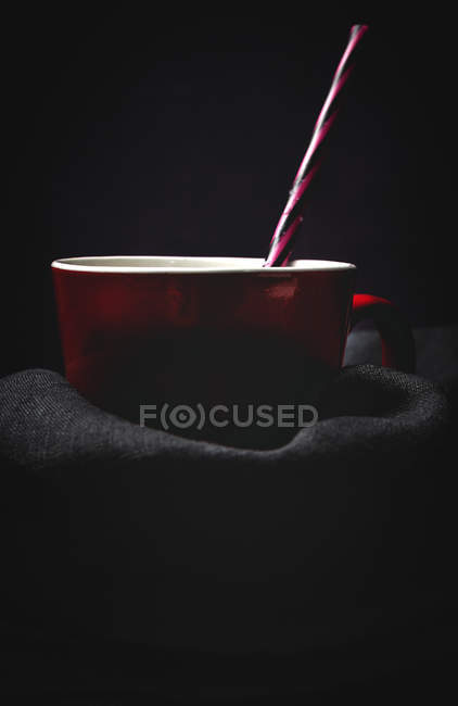 Tazza di latte bianco con paglia brillante a righe su tavola su fondo nero — Foto stock
