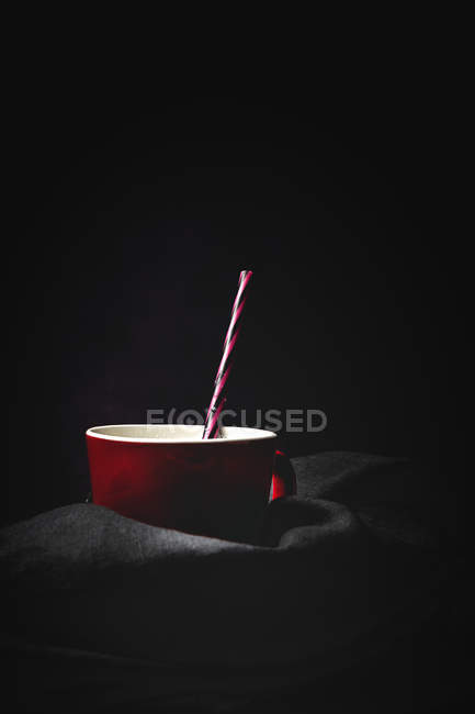 Cup of white milk with bright striped straw on table over black background — Stock Photo