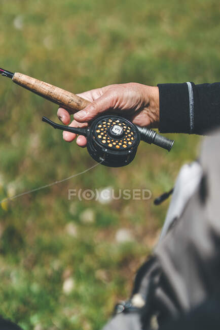 Crop man tenendo attrezzatura da pesca moderna mentre in piedi sulla riva del fiume erbosa alla luce del giorno — Foto stock