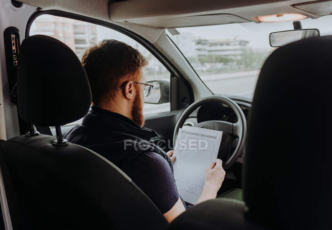 Man focusing and checking documents while sitting behind steering wheel in car cabin during daytime on blurred background — Stock Photo