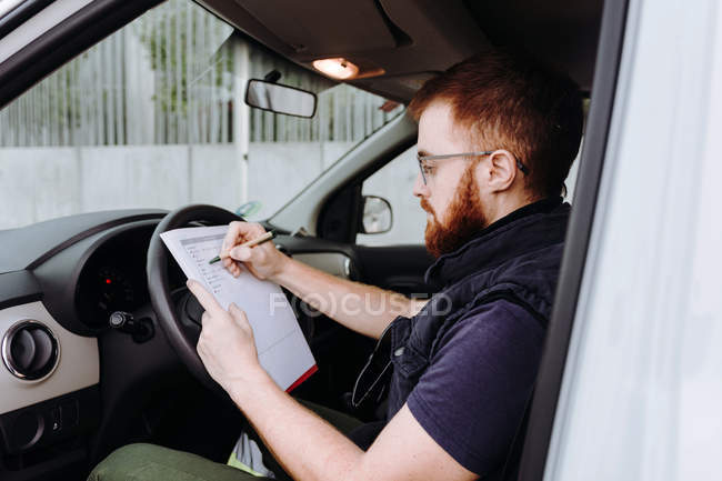 Man focusing and checking documents while sitting behind steering wheel in  car cabin during daytime on blurred background — express, papers - Stock  Photo | #312661362