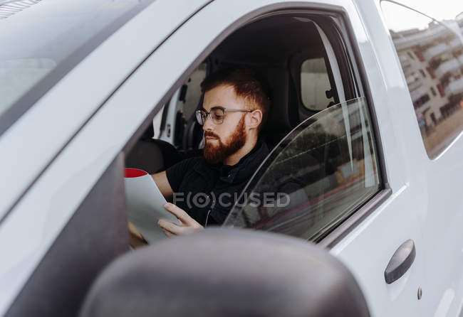 Uomo messa a fuoco e controllo dei documenti mentre seduto dietro il volante in cabina di guida durante il giorno su sfondo sfocato — Foto stock