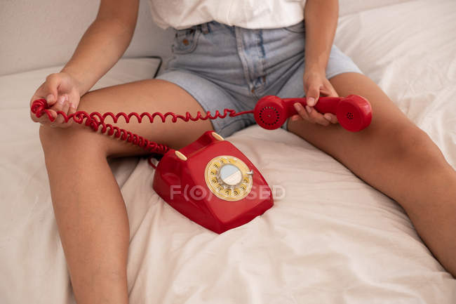Imagen recortada de la mujer jugando con el auricular rojo en el teléfono retro después de terminar la conversación en la cama - foto de stock