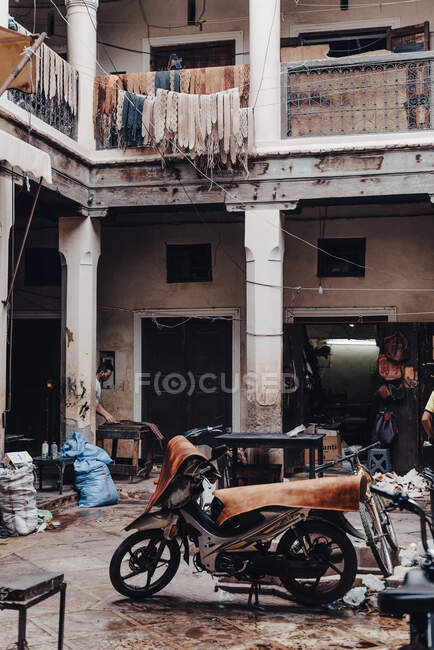 Motociclo invecchiato con pezzi di tessuto parcheggiati nel cortile di un edificio esposto alle intemperie con vestiti asciutti sulla strada di Marrakech, Marocco — Foto stock