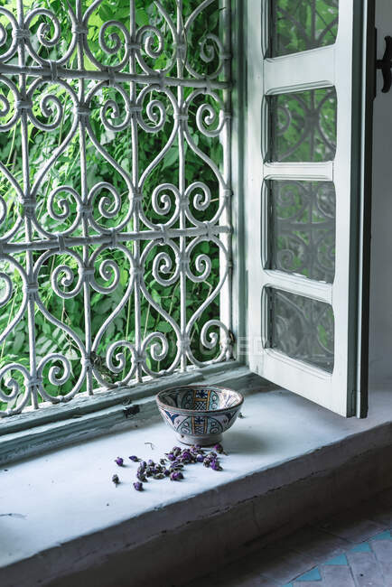 Piccoli boccioli di fiori secchi e ciotola ornamentale collocati vicino alla finestra aperta all'interno della tradizionale casa araba a Marrakech, Marocco — Foto stock