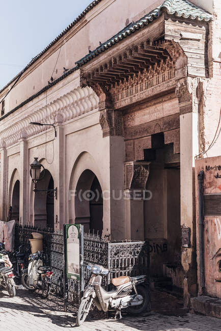 Shabby scooters motor estacionado na rua fora do edifício árabe tradicional no dia ensolarado na rua de Marraquexe, Marrocos — Fotografia de Stock