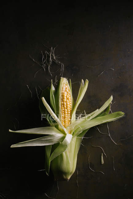 Top view of fresh ripe corn in green leaves on black table — Stock Photo