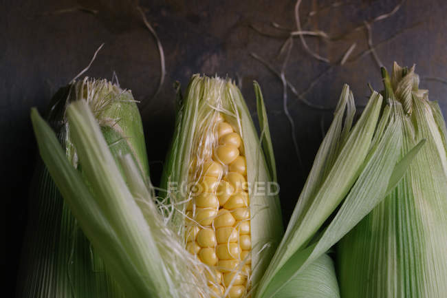 Vue du dessus des épis de maïs frais mûrs en feuilles vertes sur table noire — Photo de stock