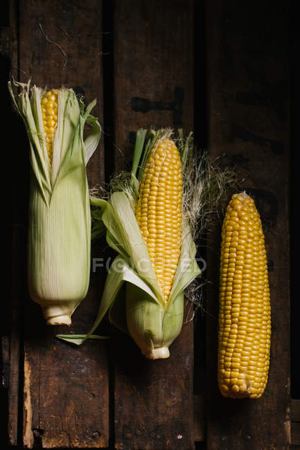 Vue de dessus du maïs frais mûr dans des feuilles vertes sur une caisse en bois — Photo de stock