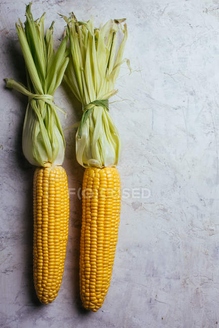 Свіжа стигла кукурудза в зеленому листі на мармуровому столі — стокове фото
