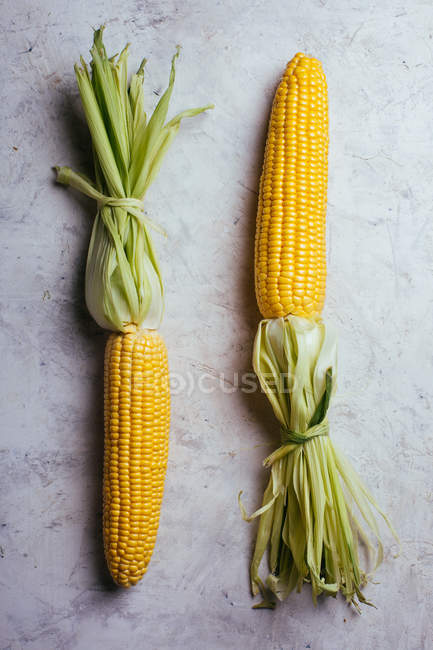Свіжа стигла кукурудза в зеленому листі на мармуровому столі — стокове фото