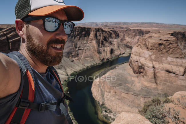 Cheerful tourist in sunglasses with backpack taking selfie on background of stony canyon and river in USA — Stock Photo