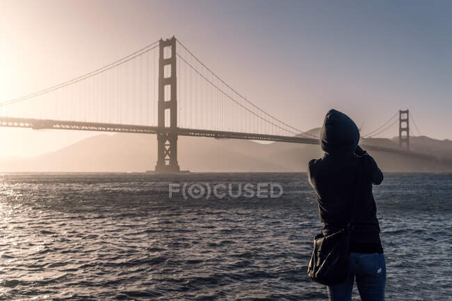 Visão traseira da pessoa de jaqueta com capuz olhando para a ponte longa sob o mar ondulado interminável nos EUA — Fotografia de Stock