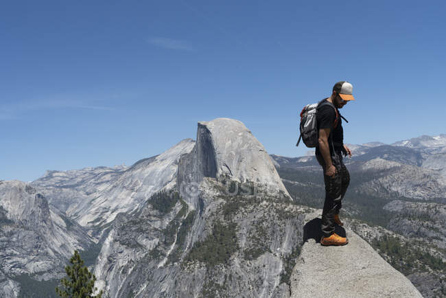Vista laterale dell'uomo casual in occhiali da sole con zaino in piedi e lo sguardo sulla cima della collina rocciosa nella giornata di sole negli Stati Uniti — Foto stock