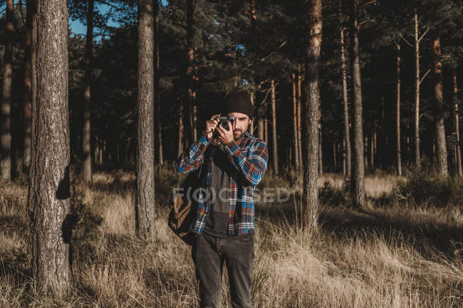 Уверенный фотограф фотографируется с камерой в солнечном лесу — стоковое фото